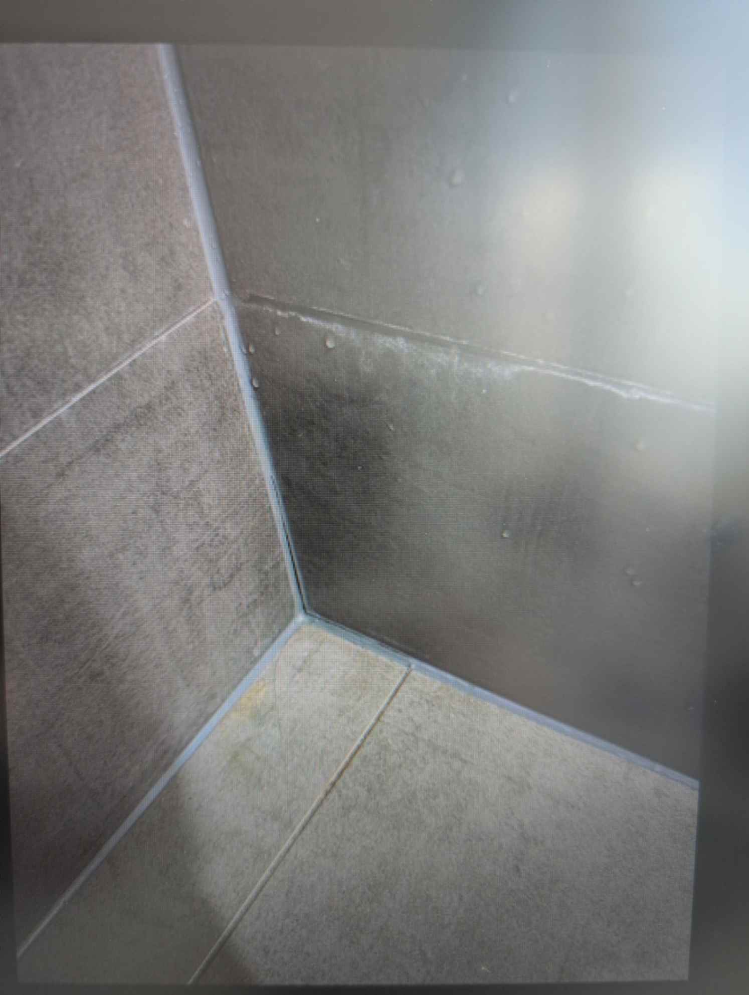 Tiled shower corner with grey tiles.