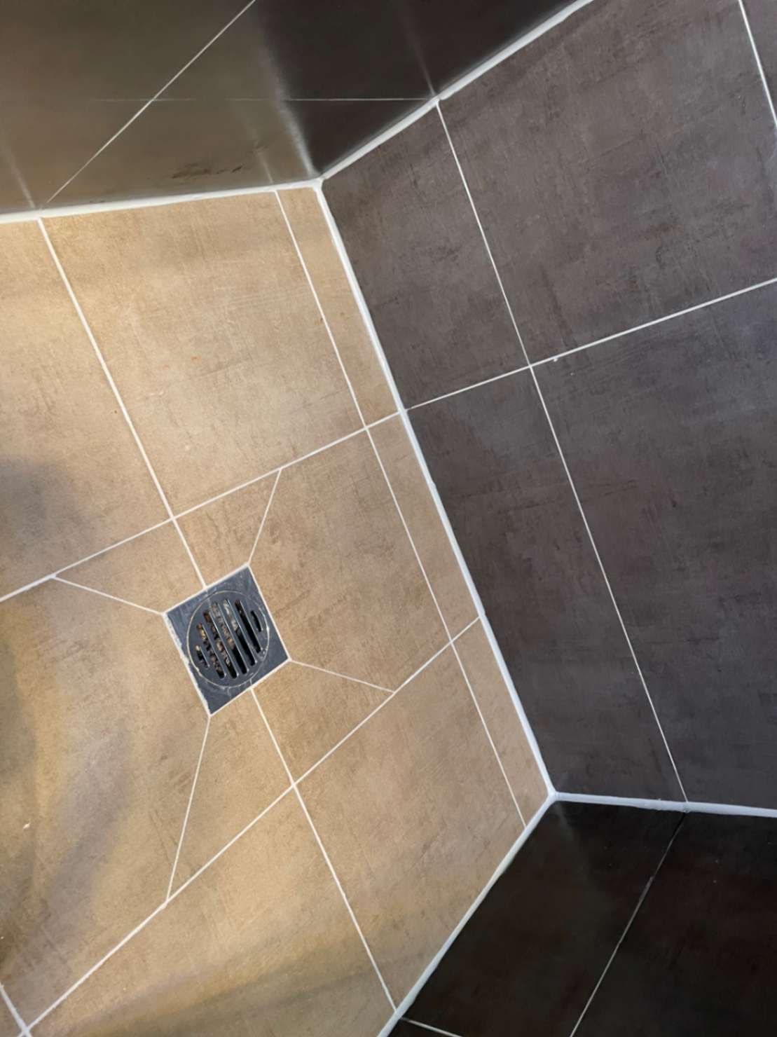 Shower floor with beige and grey tiles and drain.
