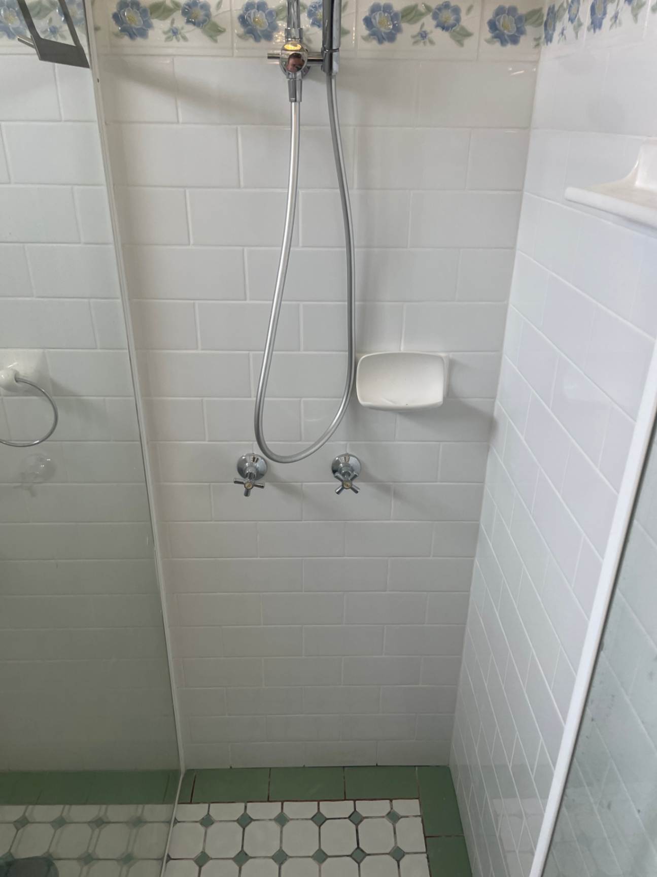 Shower stall with white tiles and handheld shower head.