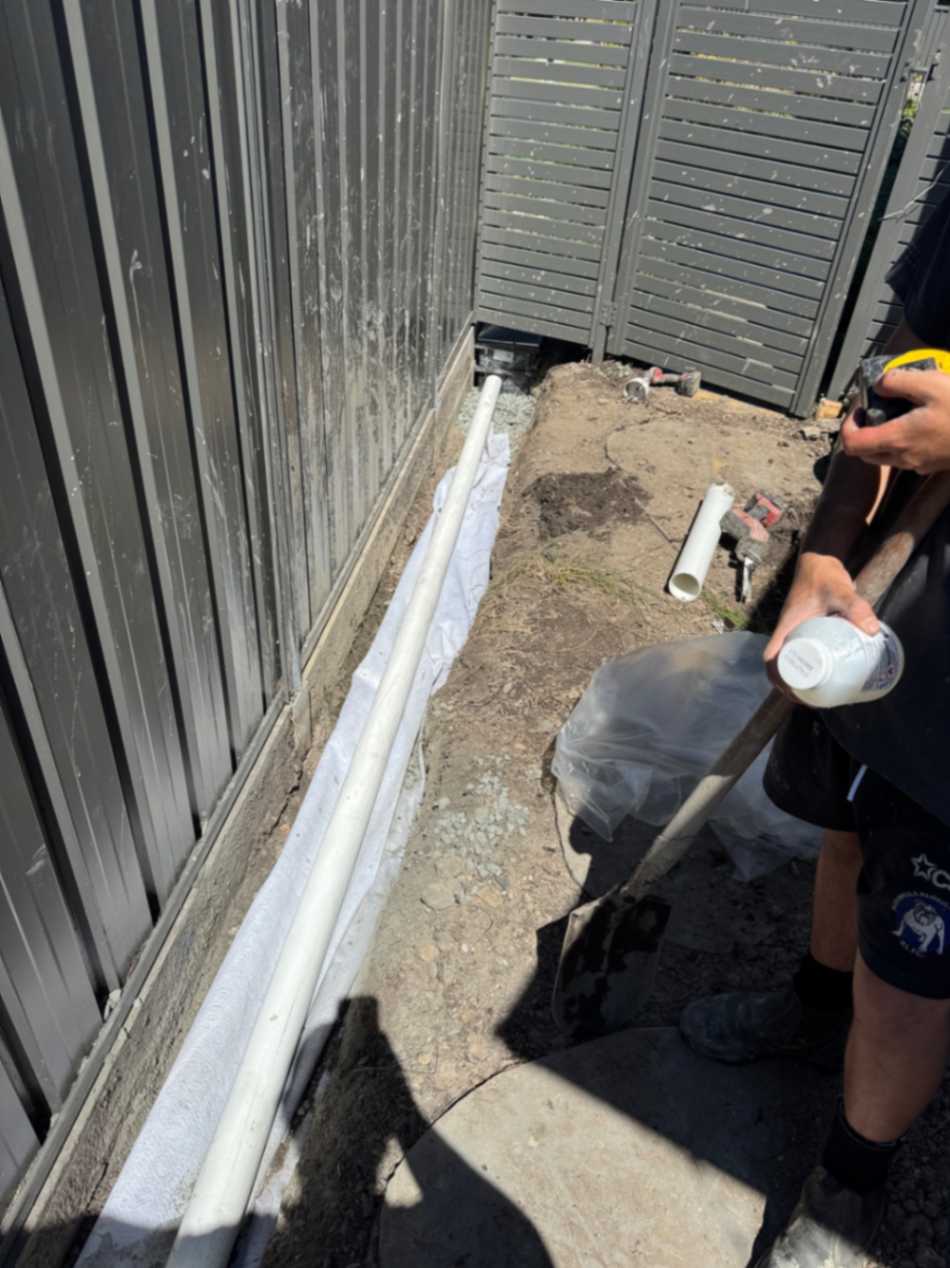 Plumber installing drainage pipe along fence.