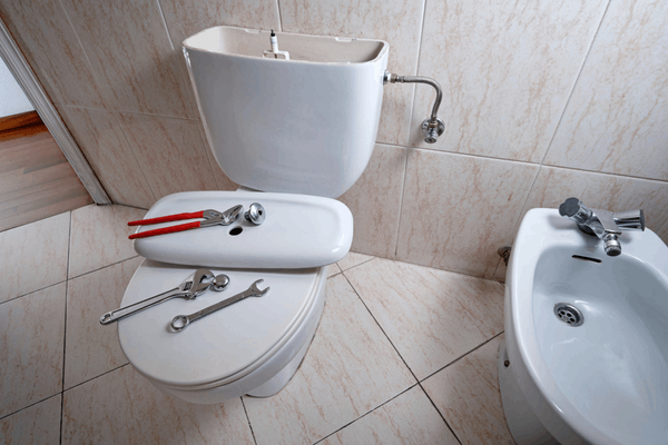Plumbing spanners and wrenches resting on a toilet during cistern refill repairs